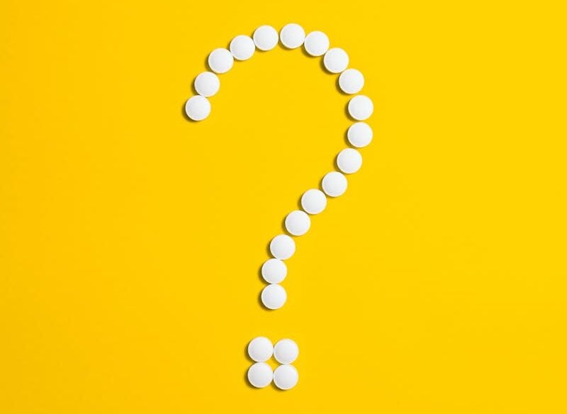 White pills arranged in a question mark shape on a bright yellow background, symbolizing medical queries.